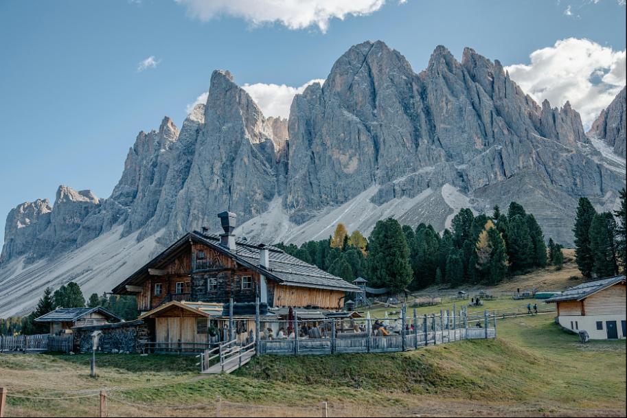 Tradycyjna górska chata w Dolomitach z postrzępionymi skalistymi szczytami i lasem sosnowym w tle – Włochy