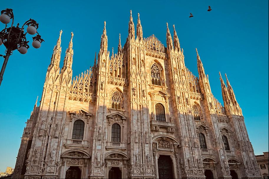 Katedra w Mediolanie (Duomo di Milano) – gotycka fasada ze strzelistymi wieżyczkami oświetlona złotym światłem zachodzącego słońca